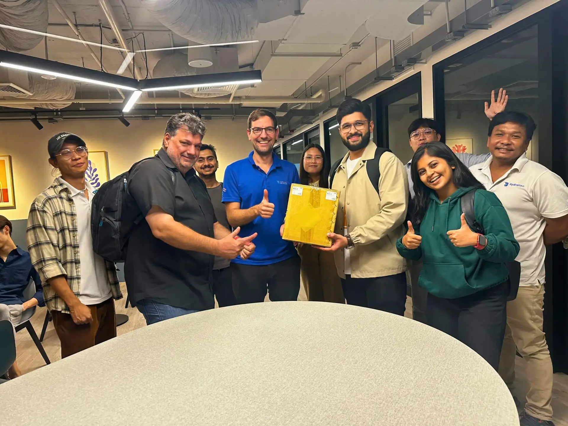 A group photo of the HydroNeo team, posing together with a package in the office, showing thumbs up and smiles