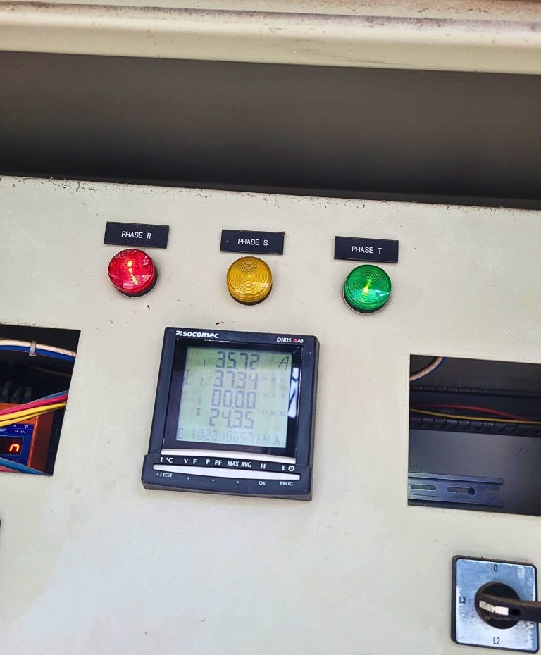 Electrical control panel with phase indicator lights and a digital power meter displaying voltage readings