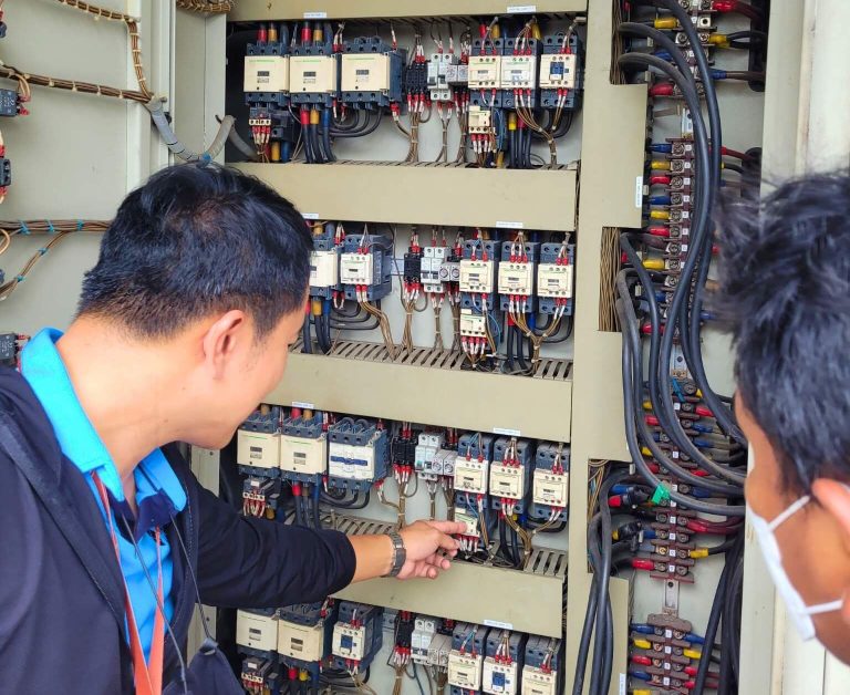 HydroNeo Team with the Thai Union technicians inspecting and pointing at components inside an open electrical control panel with complex wiring