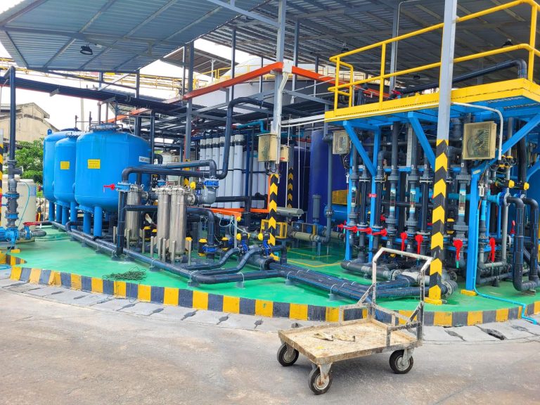 HydroNeo team visiting an industrial water treatment facility with blue filtration tanks, pipelines, and control systems under a covered structure