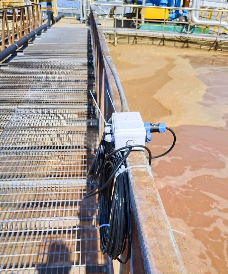 HydroNeo's Mini Controller mounted on a railing above an industrial wastewater treatment facility for smarter monitoring of water quality and better automation